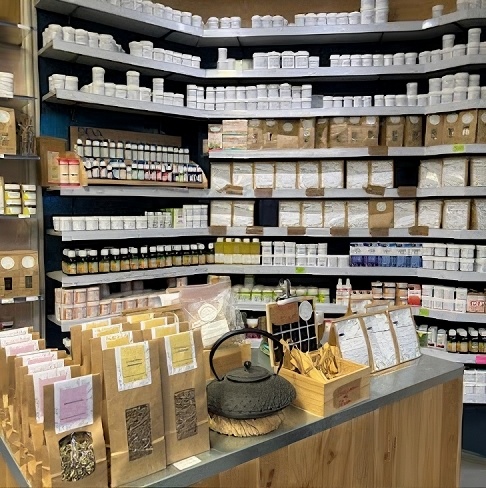 Intérieur de la Pharmacie & Herboristerie Liberté : rayonnages remplis de pots kraft de plantes, théière japonaise sur le comptoir